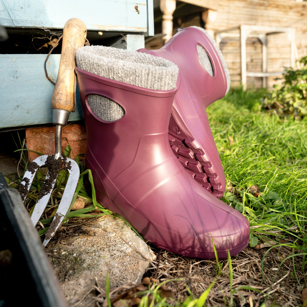 Purple rubber boots with a gardening tool on grass