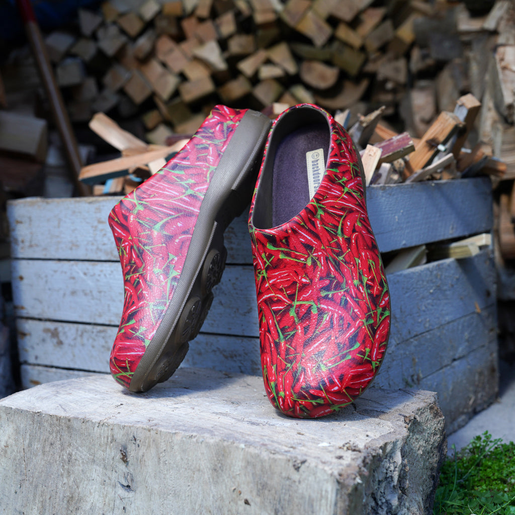 Red and green patterned gardening clogs shoes on a stone ledge with wooden logs in the background