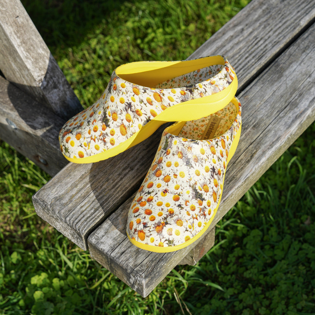 Pair of floral-patterned clogs with yellow soles on a wooden bench outdoors.