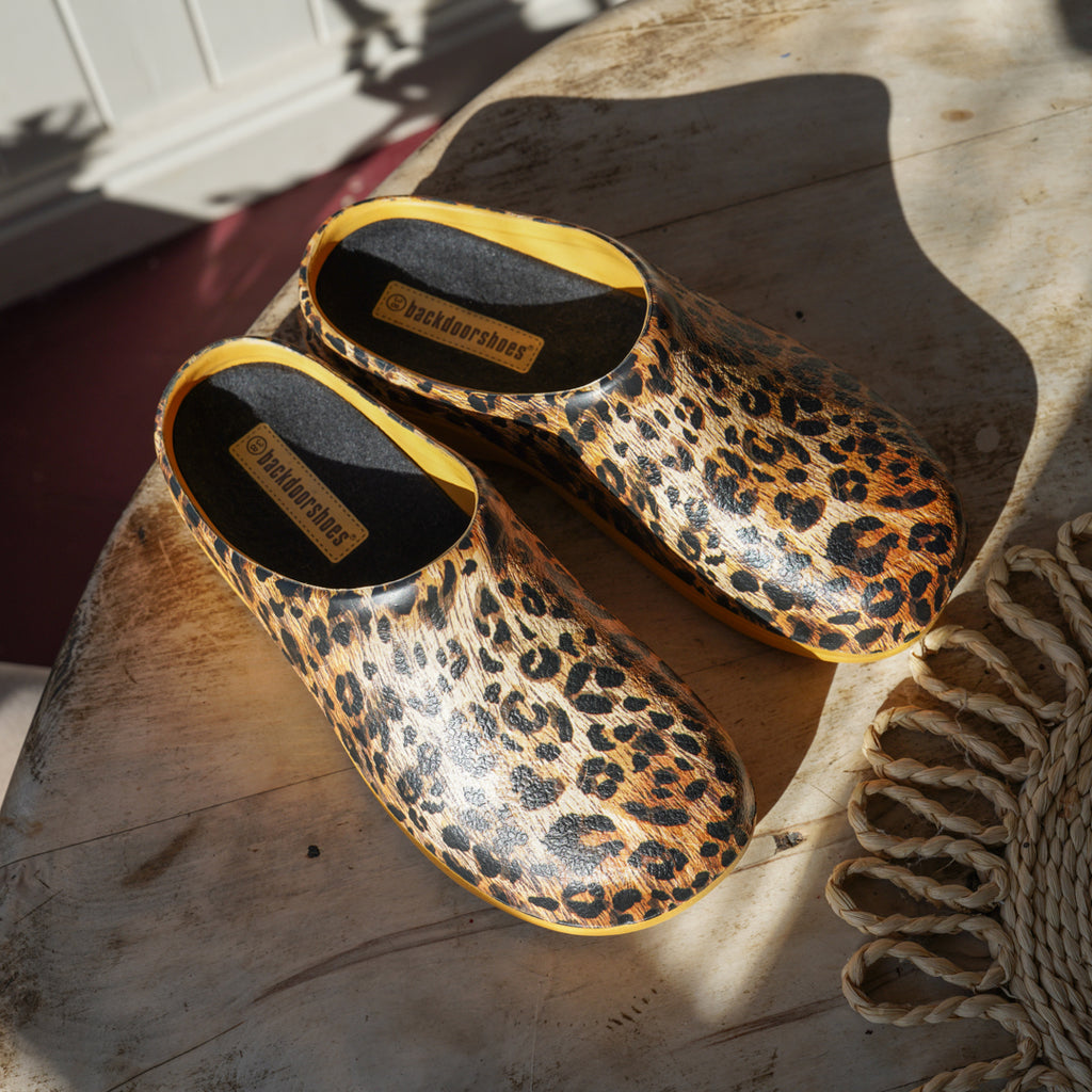 Pair of leopard print clogs on a wooden surface with a brand label visible.